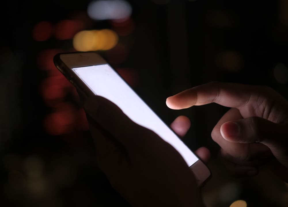 A hand on a phone in the dark with city lights behind it