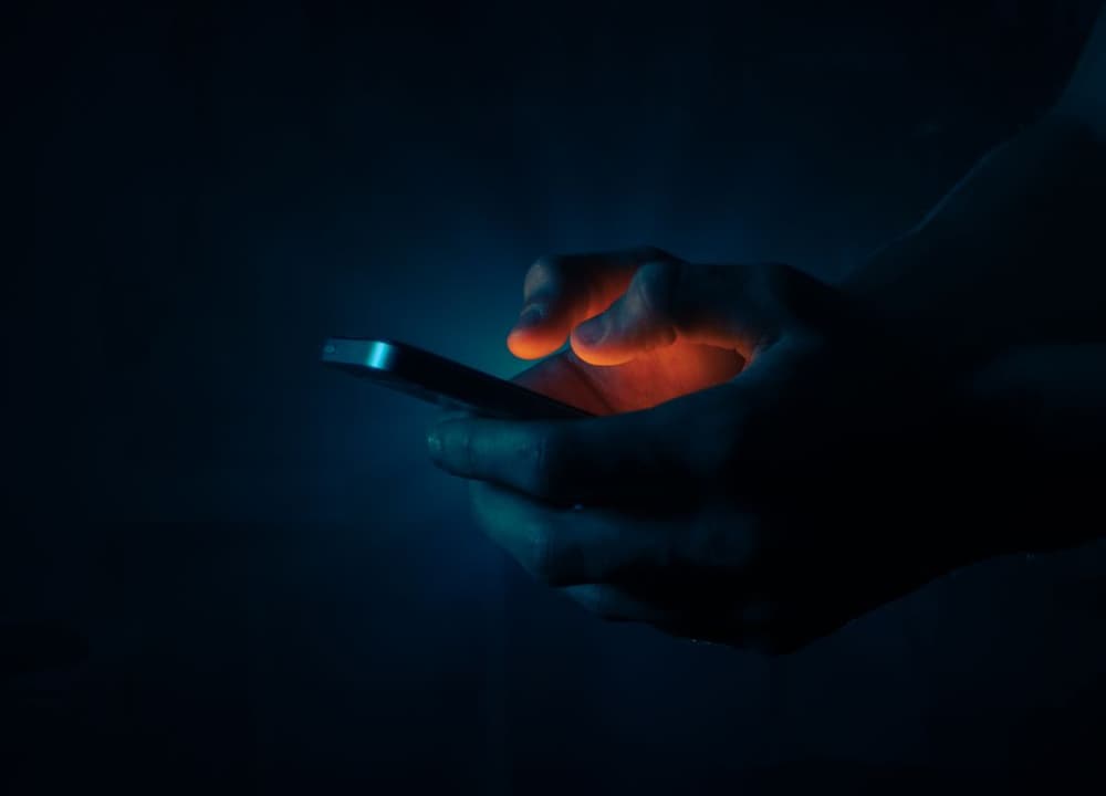 Hands holding a phone in the dark, lit only by its screen